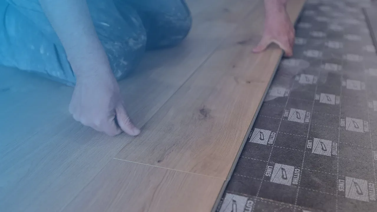 Ein Mann kniet auf einem teilweise verlegtem Laminatboden in Holzoptik und drückt die zuletzt verlegte Paneel fest.