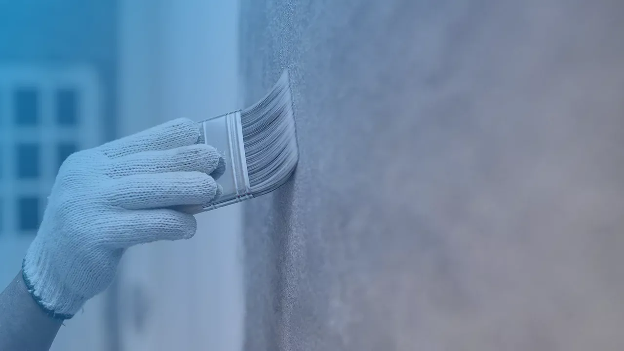Ein Foto von einer Hand mit einem Pinsel die Farbe an einer Wand verstreicht.